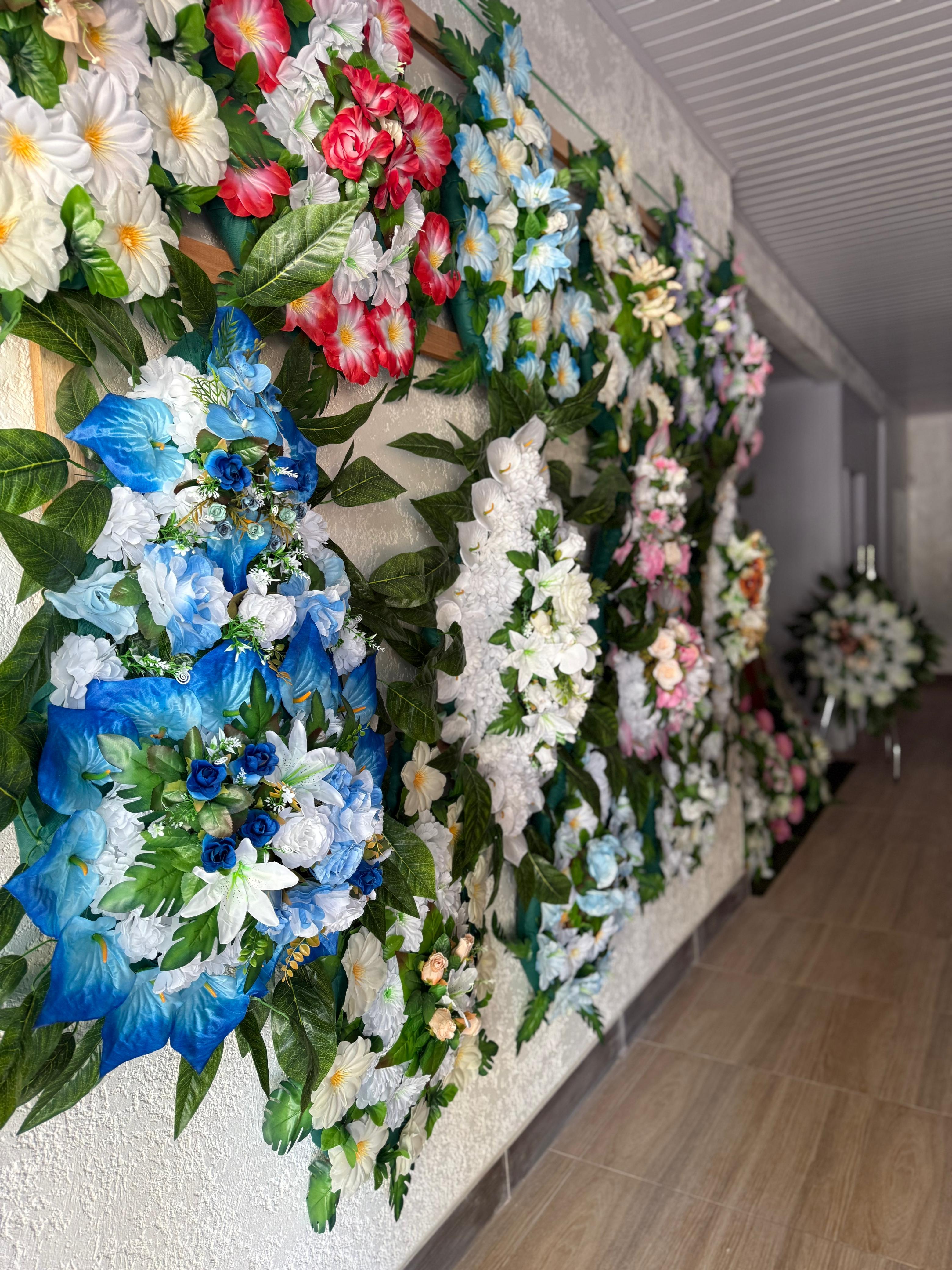parede coberta com arranjos de flores artificiais coloridas em corações e círculos, num corredor interno de salão  — tex